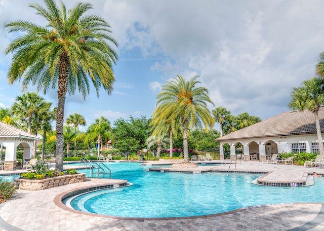 A pool with palm trees and a gazebo in the background.